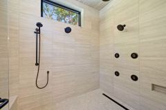 Luxury curbless walk-in shower with multiple shower heads, body sprays, built-in bench, and custom tile niches in The Vandoren primary bathroom in Liberty Township, Ohio.