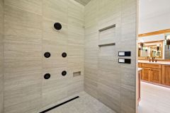 Luxury curbless walk-in shower with multiple shower heads, body sprays, built-in bench, and custom tile niches in The Vandoren primary bathroom in Liberty Township, Ohio.