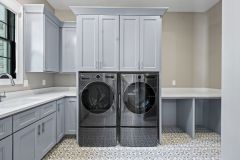 Custom laundry room with built-in washer and dryer, cabinetry, utility sink, pendant lighting, and decorative tile flooring in The Vandoren home in Liberty Township, Ohio.