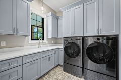 Custom laundry room with built-in washer and dryer, cabinetry, utility sink, pendant lighting, and decorative tile flooring in The Vandoren home in Liberty Township, Ohio.
