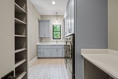 Custom laundry room with built-in washer and dryer, cabinetry, utility sink, pendant lighting, and decorative tile flooring in The Vandoren home in Liberty Township, Ohio.