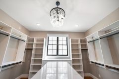 Custom walk-in closet with quartz island countertop, chandelier, built-in cabinetry, and specialty storage in The Vandoren luxury primary suite in Liberty Township, Ohio.