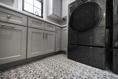 Custom laundry room with built-in washer and dryer, cabinetry, utility sink, pendant lighting, and decorative tile flooring in The Vandoren home in Liberty Township, Ohio.