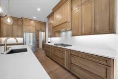 Wood Stained Kitchen Cabinetry To Ceiling With White Quartz Slab Backsplash