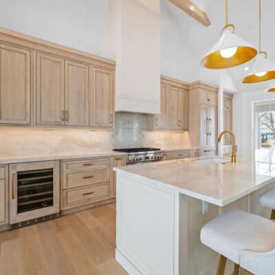 Kitchen with 2 cabinet colors and large island and backsplash using Taj Mahal granite, pendant lighting and custom hood with apron front