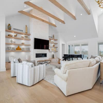 Great Room with Suspended Truss Beams, Stack Stone Fireplace and Floating Open Shelves of White Oak