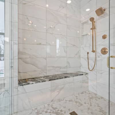 Glass Front and Side Shower With Bench and Gold Plumbing Fixtures
