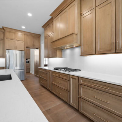 Wood Stained Kitchen Cabinetry To Ceiling With White Quartz Slab Backsplash and Black Island Cabinetry