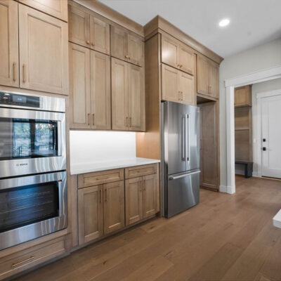 Appliance Wall In Custom Home Kitchen Wood Stained Kitchen Cabinetry To Ceiling With White Quartz Slab Backsplash and Black Island Cabinetry