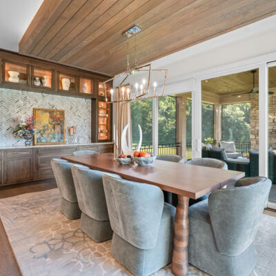 Dining Area Off Kitchen With Dropped Ceiling With Accent Lighting and Tongue and Groove Wood With Dark Built-In Cabinetry With Transom Cabinet Connecting Kitchen and Herringbone Tile Backsplash Access To Screened In Porch and Sun Deck