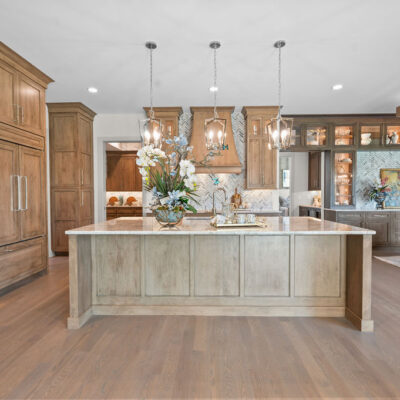 Two Toned Stained Custom Cabinetry In Kitchen With Quartzite Countertop Open To Great Room and Dining Area