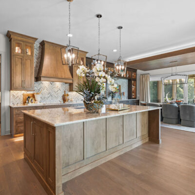 Two Toned Stained Custom Cabinetry In Kitchen With Quartzite Countertop Open To Great Room and Dining Area