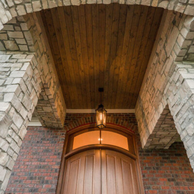 Stone Arch Covered Front Porch With Mahogany Stained Front Door With Arched Transom